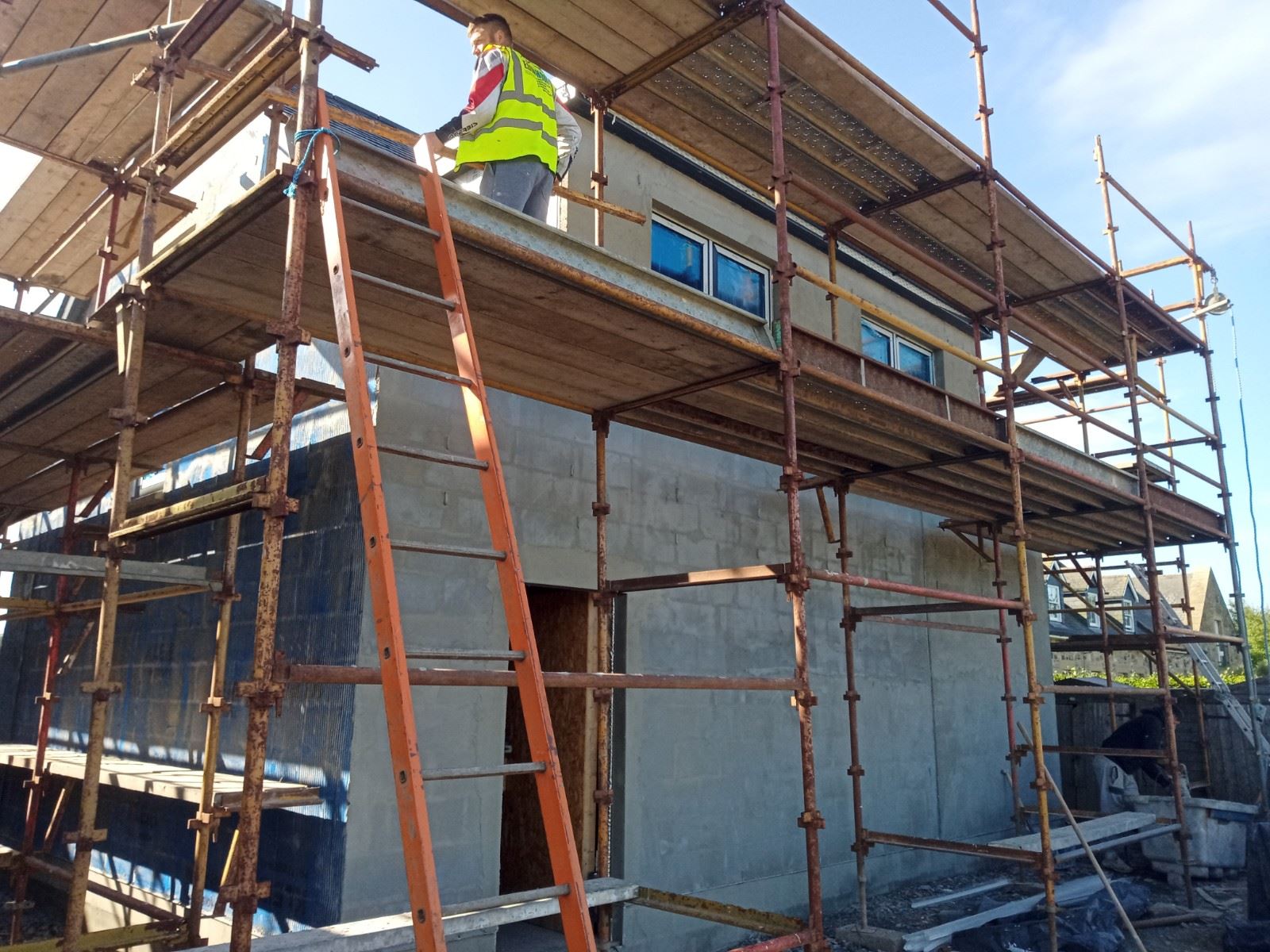 roughcast render repair on tall façade with worker at top scaffold