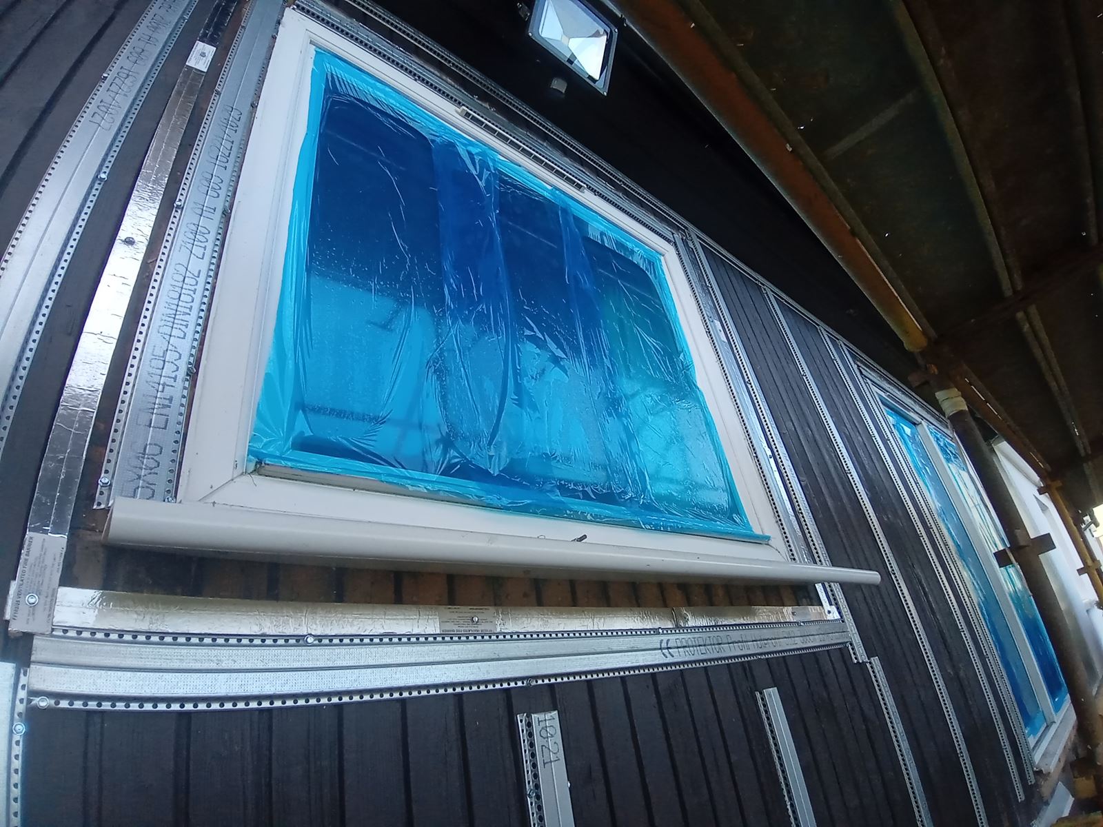roughcasting Edinburgh on wall with blue-covered window during renovation