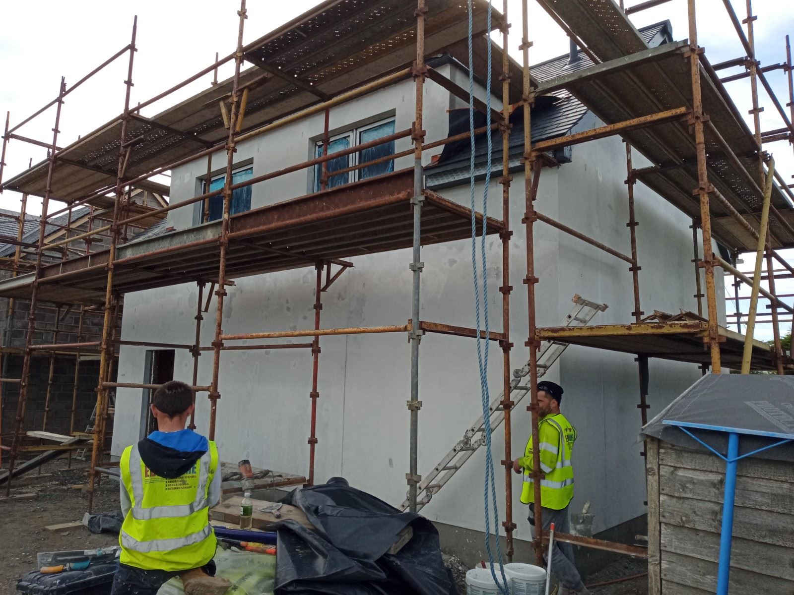 roughcast render repair carried out by workers on scaffolded wall