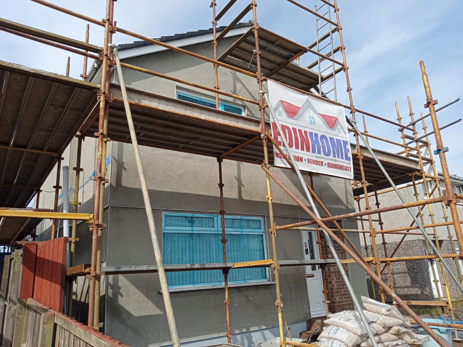 roughcast repair on house wall under scaffolding with blue window covers