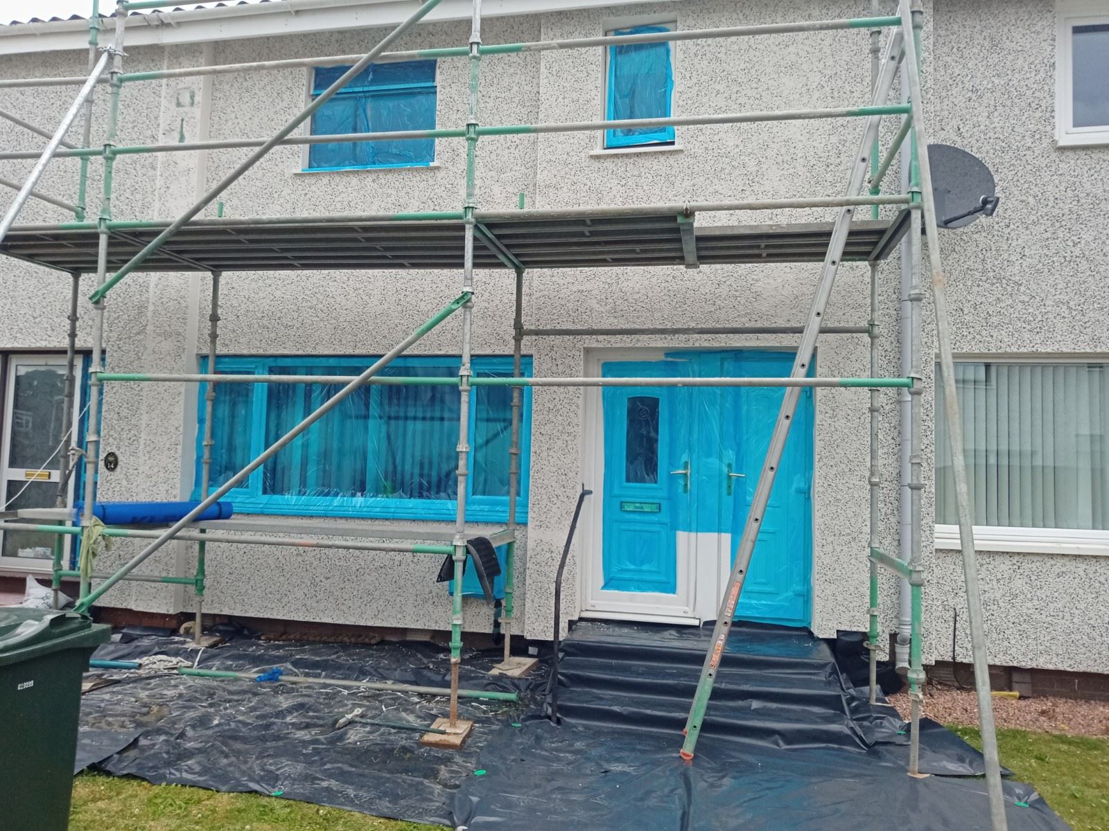roughcast repair on scaffolded home with blue window coverings