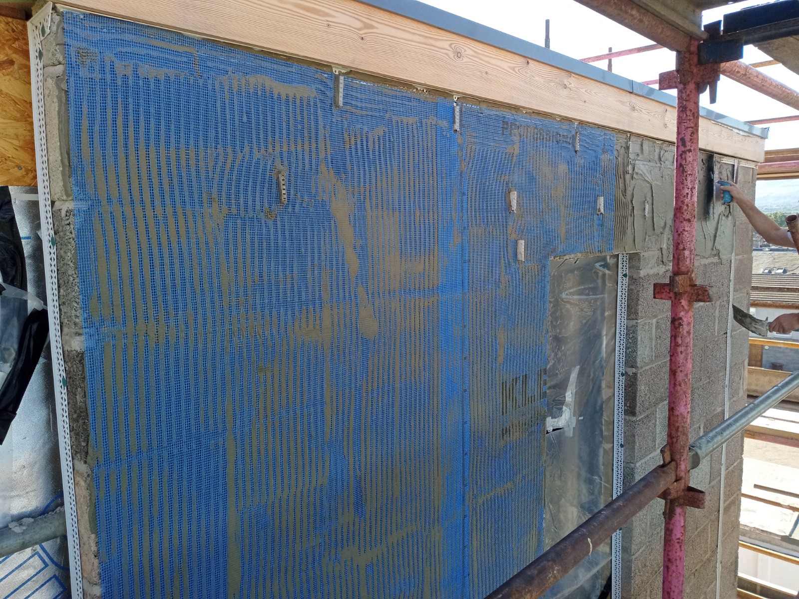 roughcast render repair on building façade with scaffold and banner