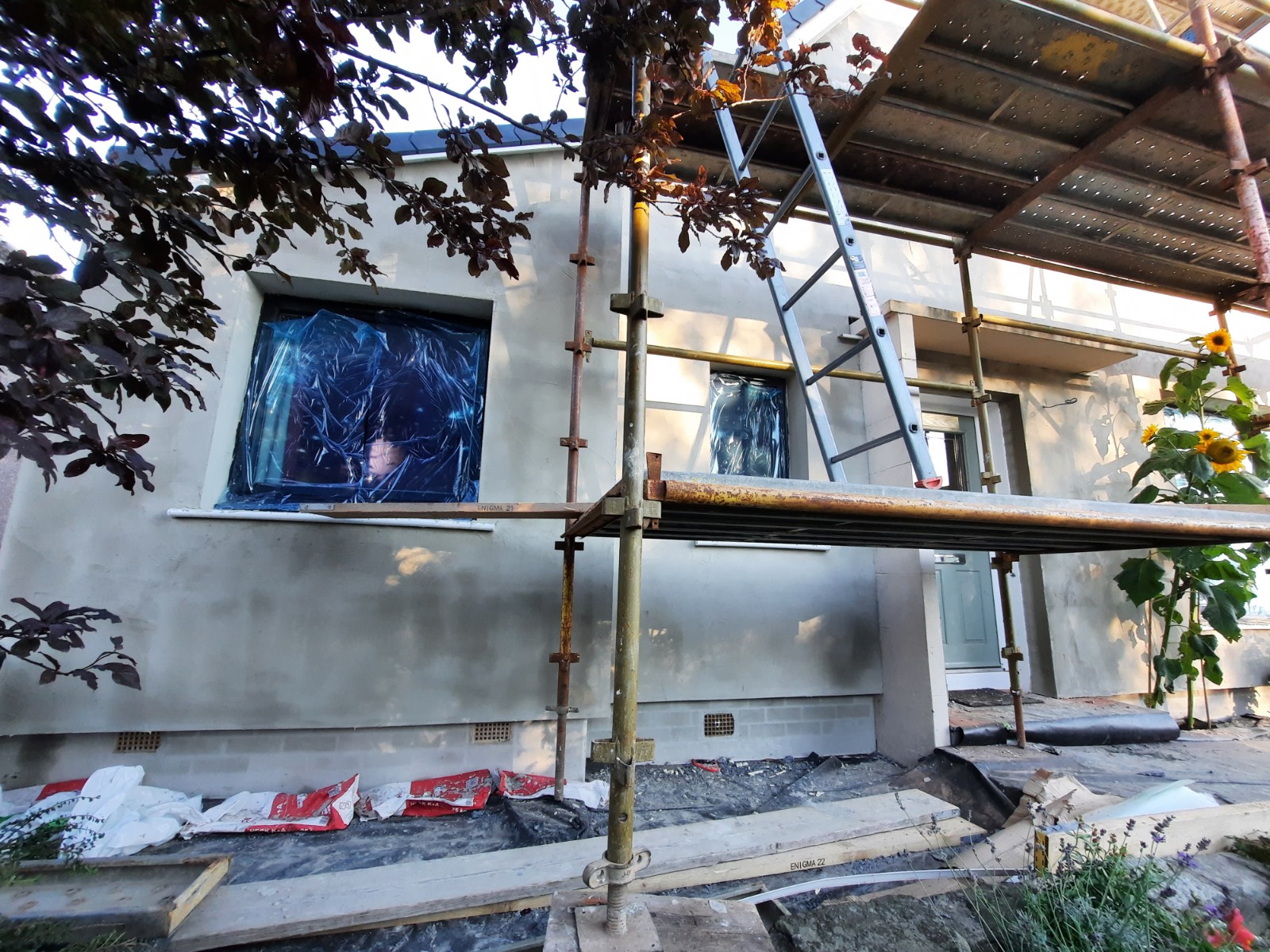 roughcast render repair on wall with blue-covered windows
