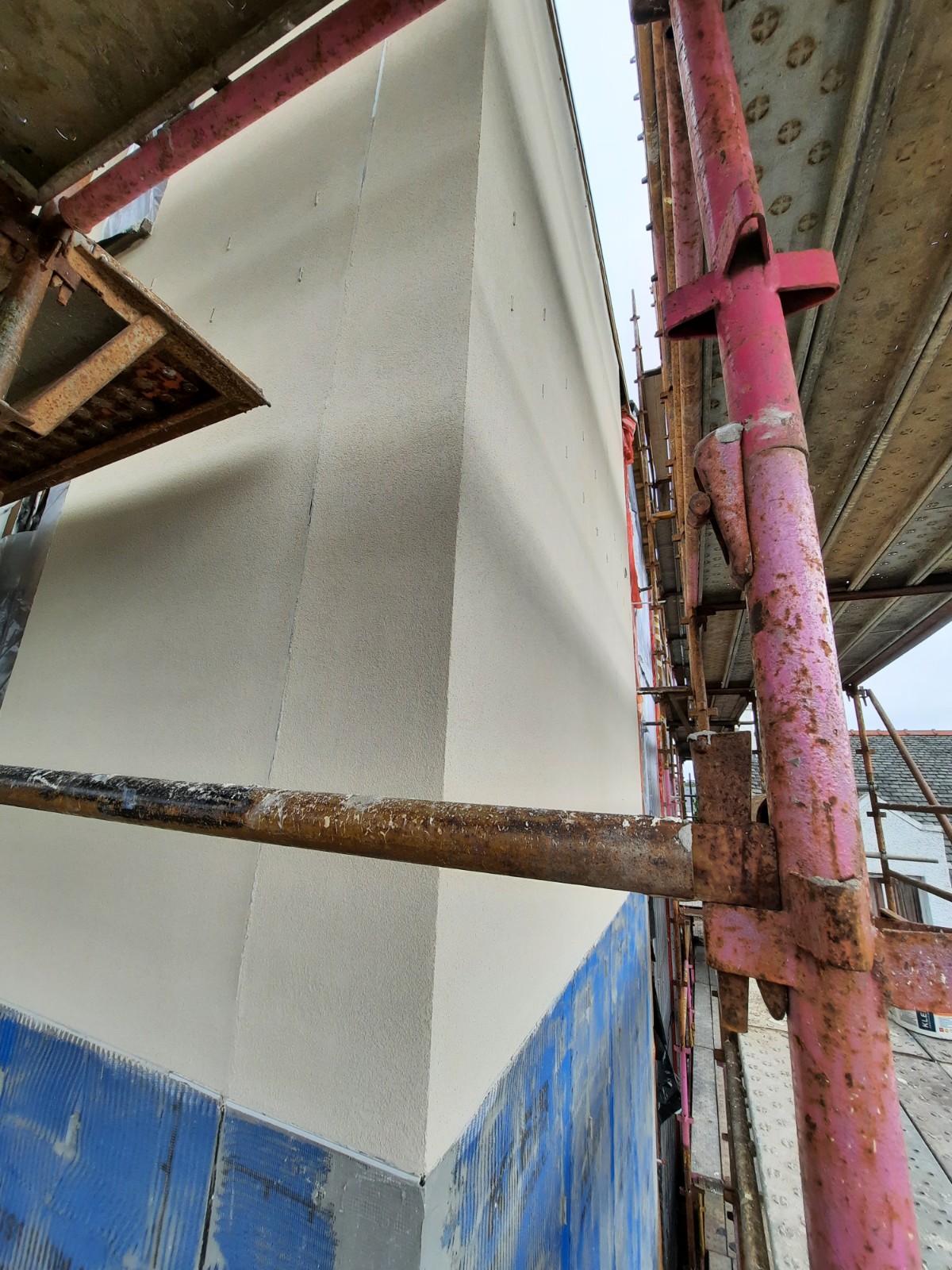 roughcasting Edinburgh on smooth white wall corner under scaffolding