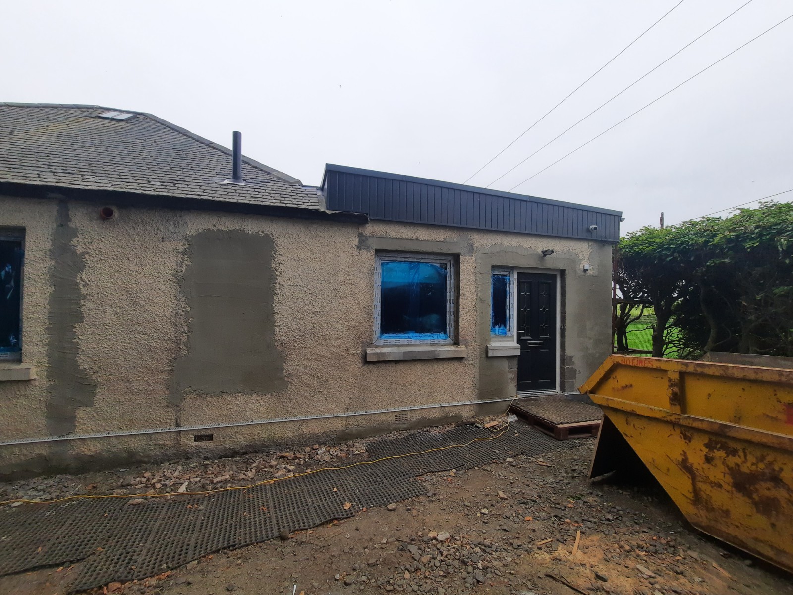 roughcast repair in progress on rear elevation with skip nearby
