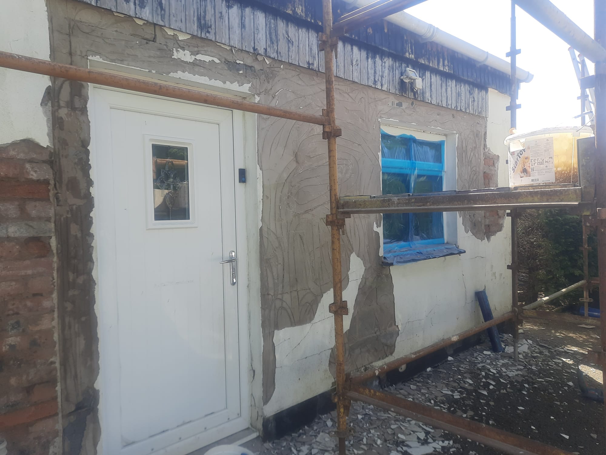 roughcast render repair in progress on bungalow rear wall with blue window cover