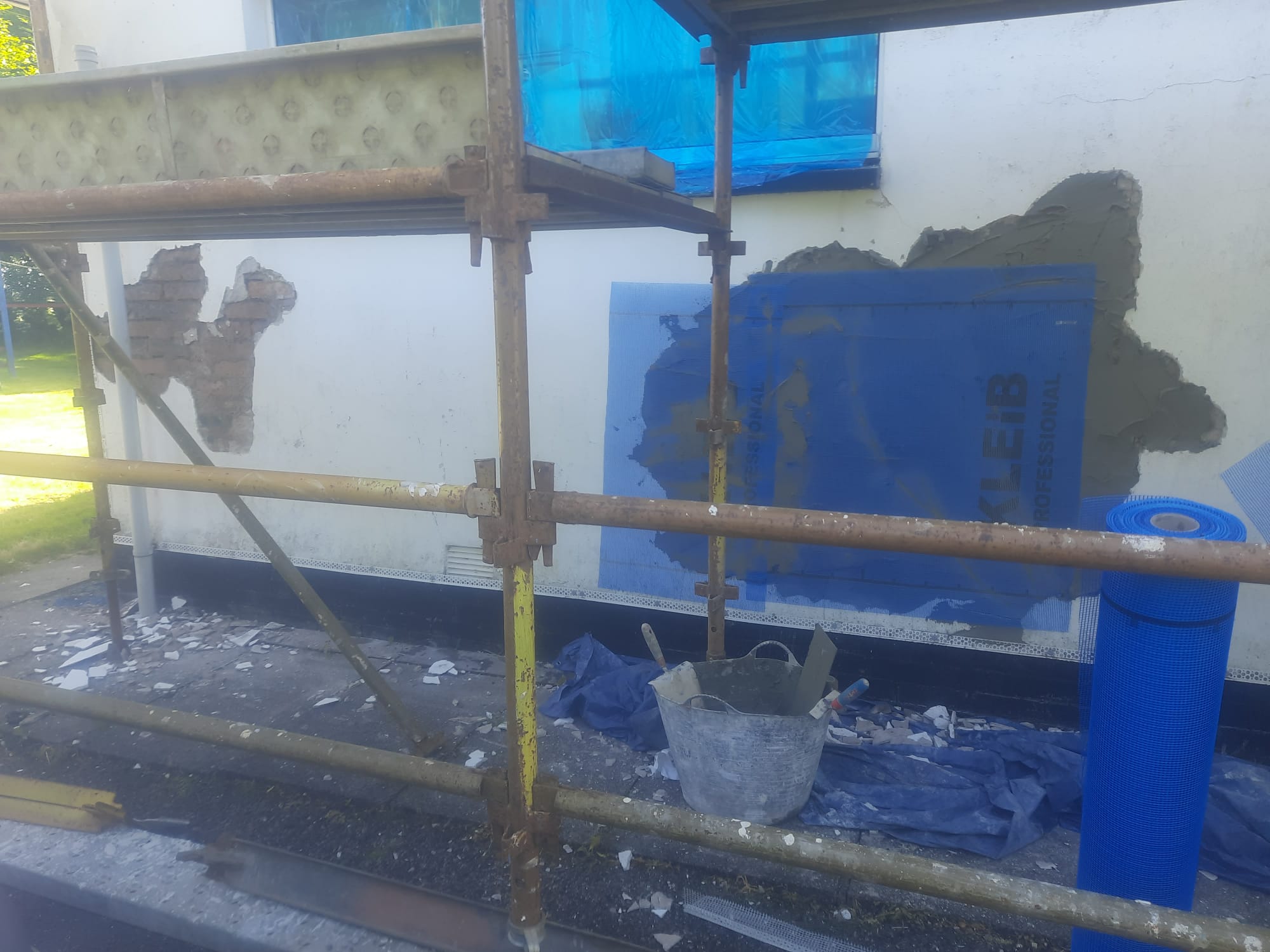 roughcast render Edinburgh on wall with blue-covered window under renovation
