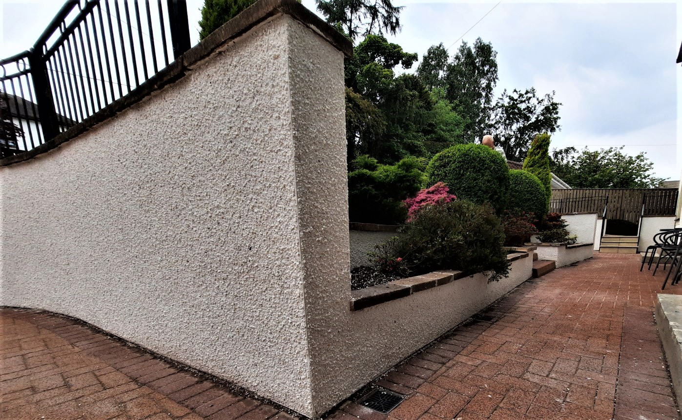 roughcast render repair on tall garden wall beside paved patio