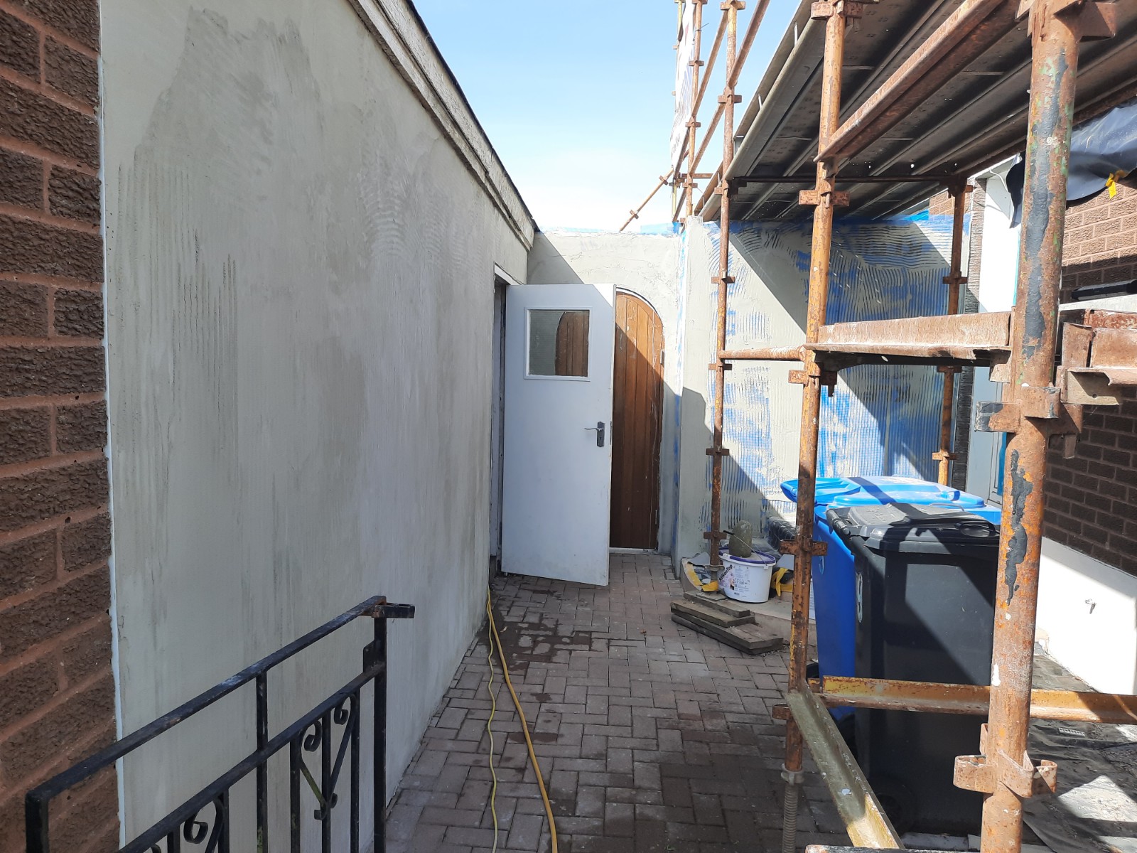 roughcast render repair along narrow pathway wall