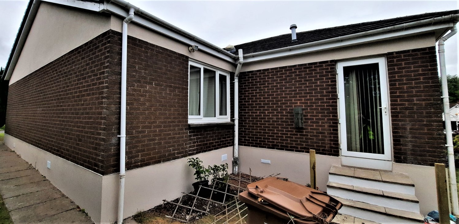 roughcast render repair on brown brick house with white trim