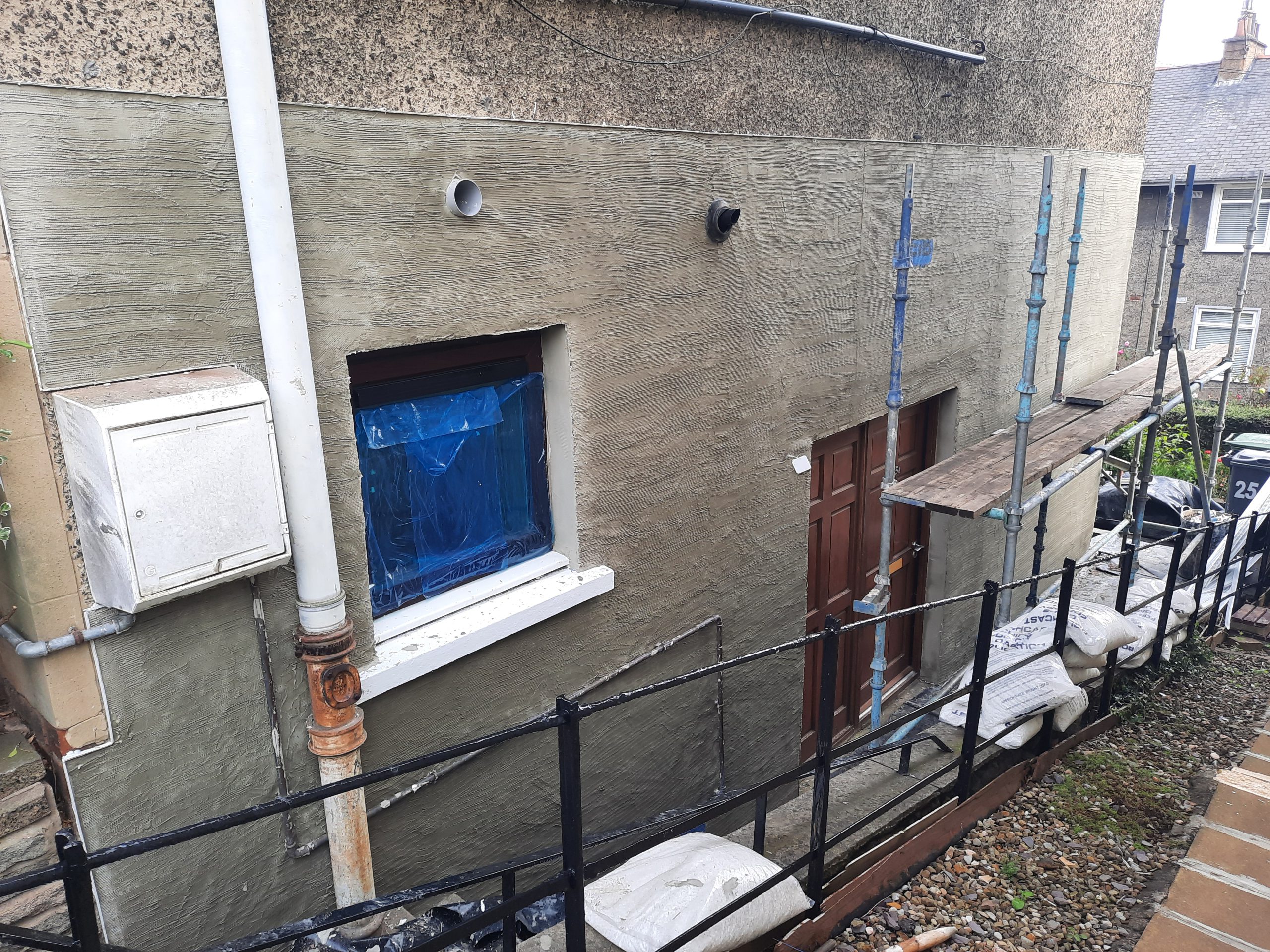 roughcasting Edinburgh on old worn façade with blue-covered window