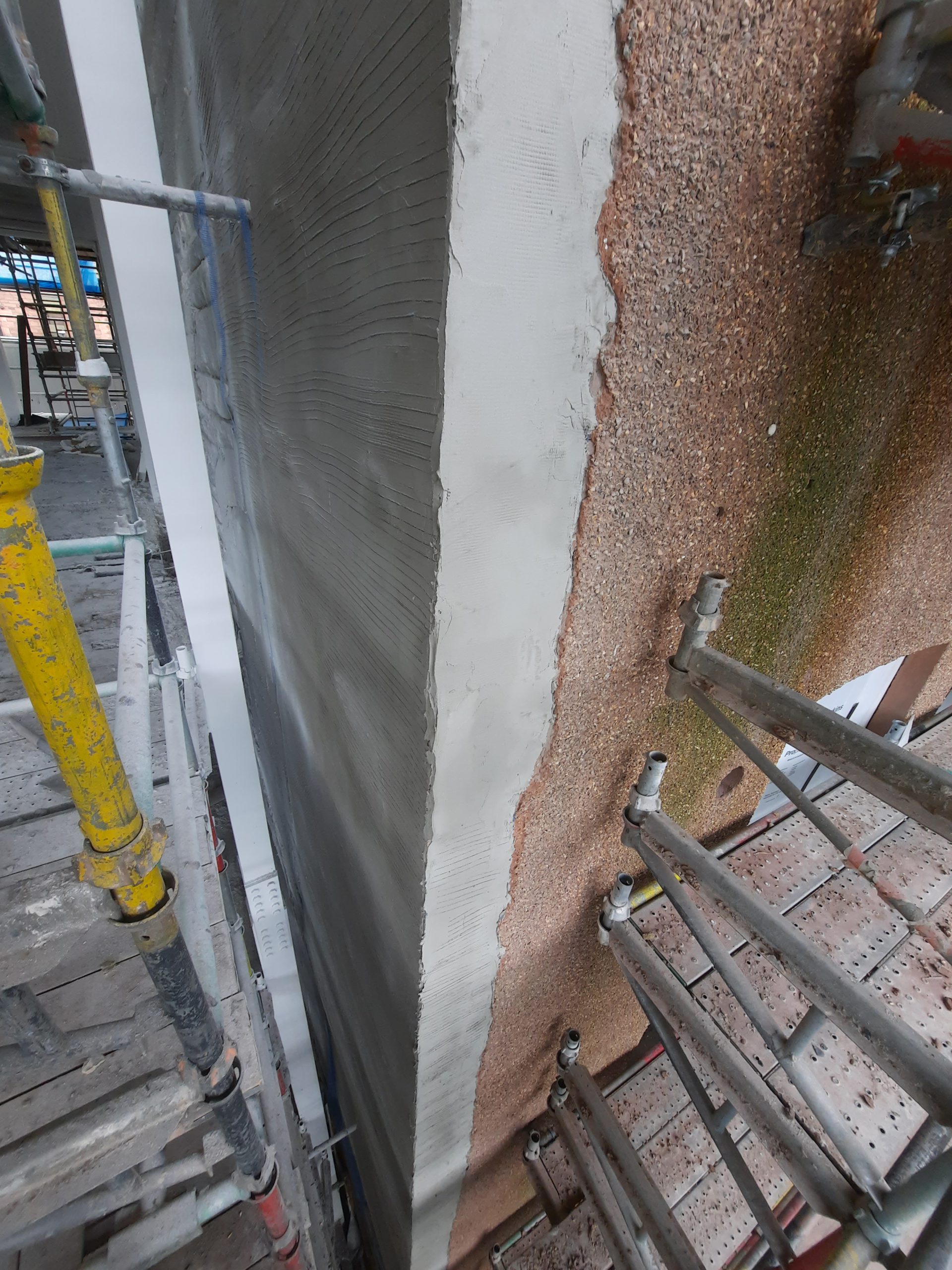 roughcast render repair on wall corner beside scaffolding