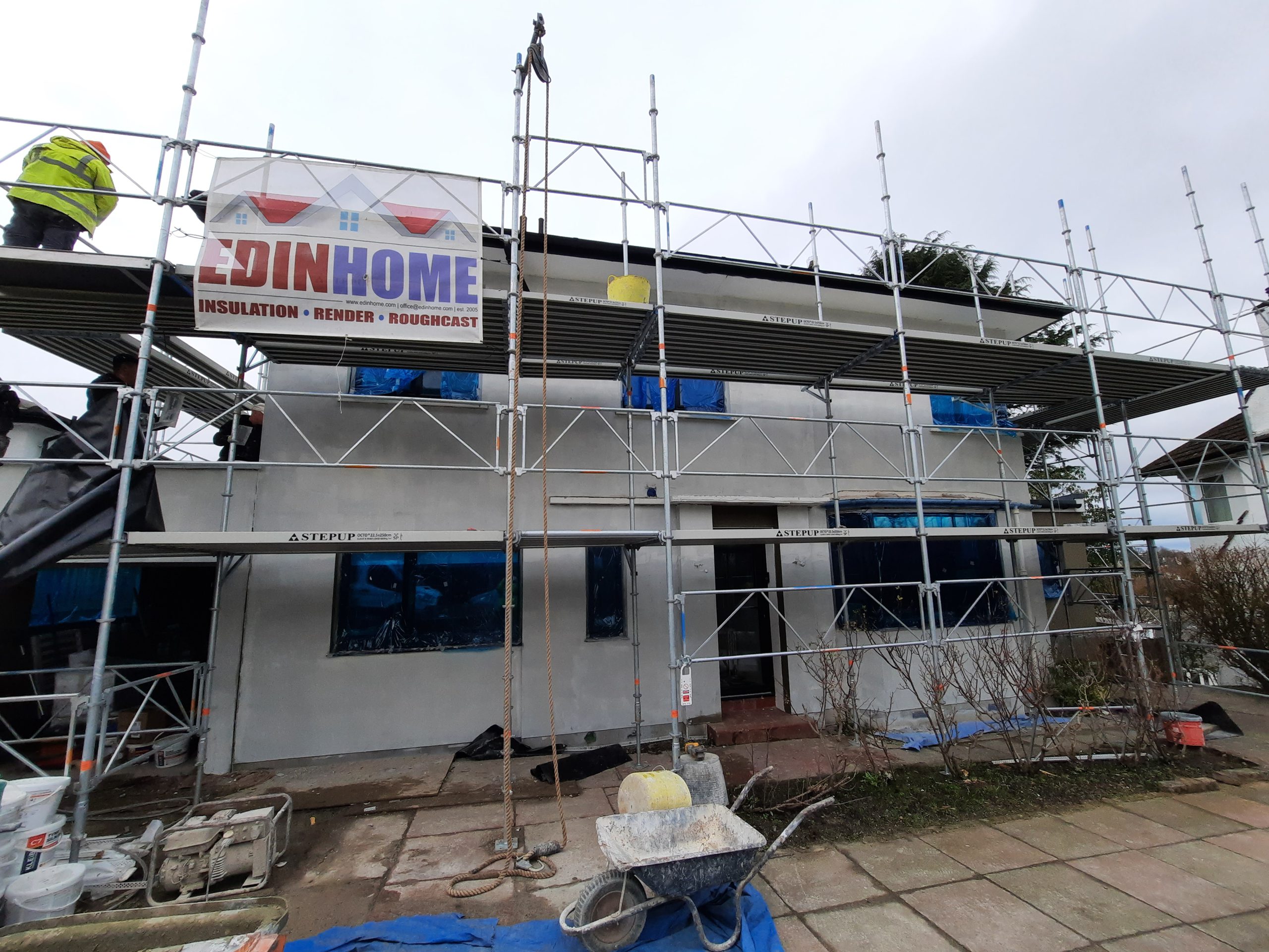 roughcast repair on scaffolded home with blue window covers