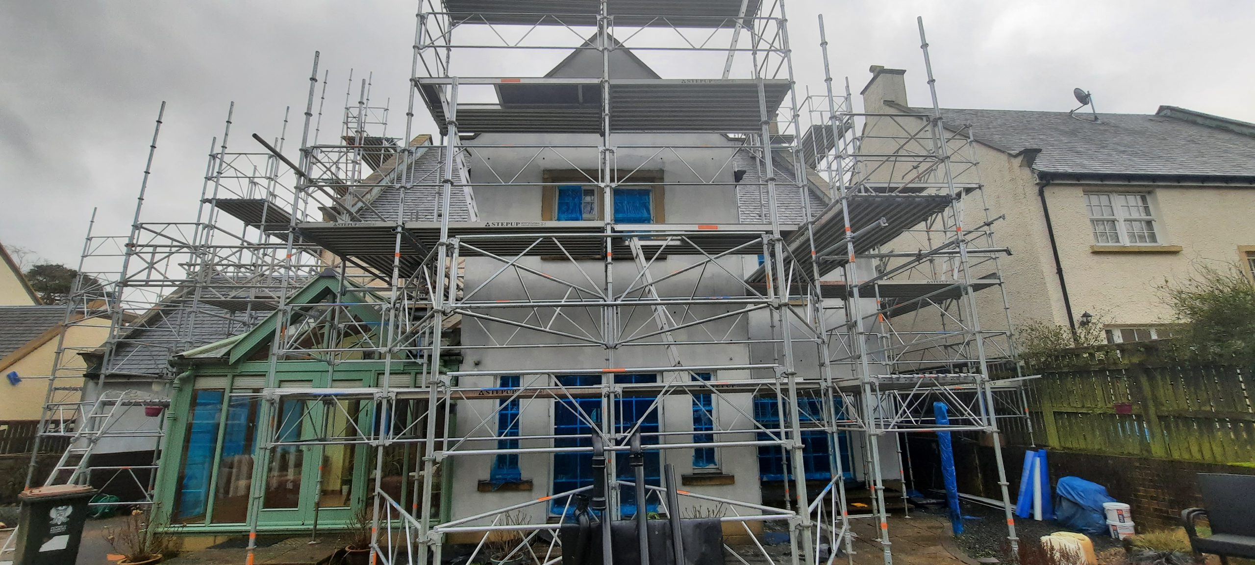 roughcast render repair on upper floor with blue-covered windows
